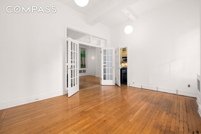 empty room with wood-type flooring, french doors, beamed ceiling, and a high ceiling