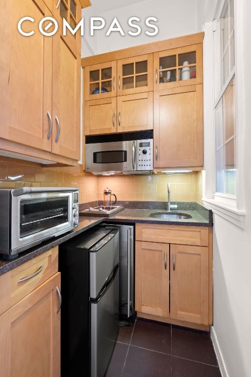 kitchen with appliances with stainless steel finishes, sink, dark stone countertops, backsplash, and dark tile patterned flooring