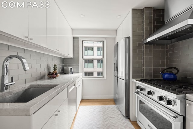 kitchen with stainless steel appliances, tasteful backsplash, wall chimney exhaust hood, white cabinets, and sink