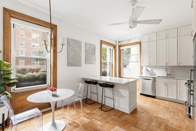 kitchen featuring stainless steel dishwasher, kitchen peninsula, a kitchen bar, sink, and white cabinets