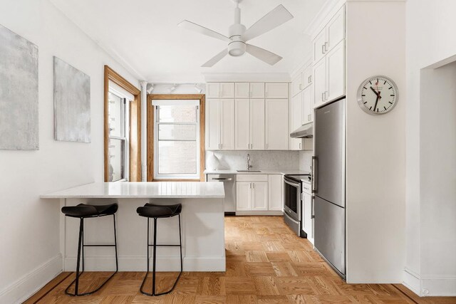 kitchen featuring kitchen peninsula, a kitchen bar, sink, stainless steel appliances, and white cabinets