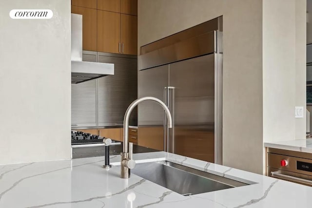 room details with light stone countertops, sink, stainless steel appliances, and range hood