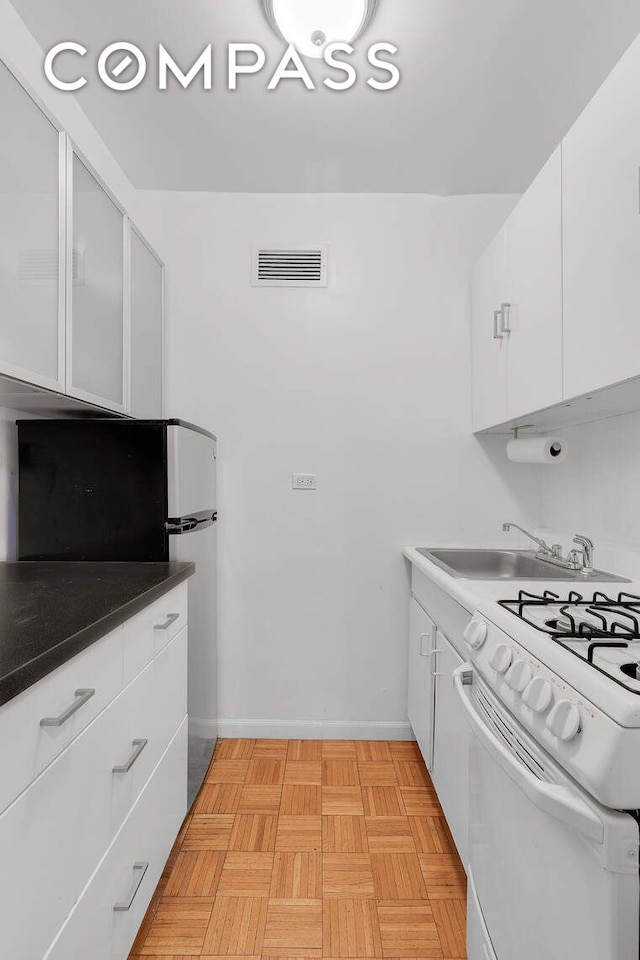 kitchen with visible vents, a sink, white gas range oven, freestanding refrigerator, and white cabinets