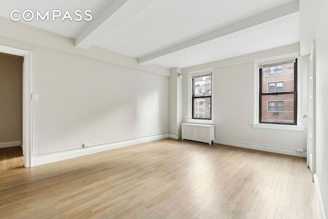 spare room featuring light wood-type flooring, radiator, beamed ceiling, and baseboards