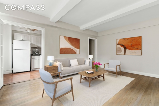 living room with light wood-type flooring, a ceiling fan, baseboards, and beam ceiling