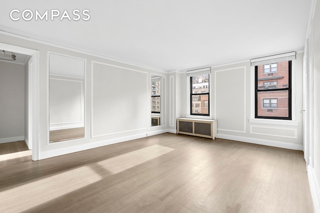 321 E 54th St Unit 10B, New York City, NY 10022 - spare room featuring a decorative wall, wood finished floors, radiator, and crown molding