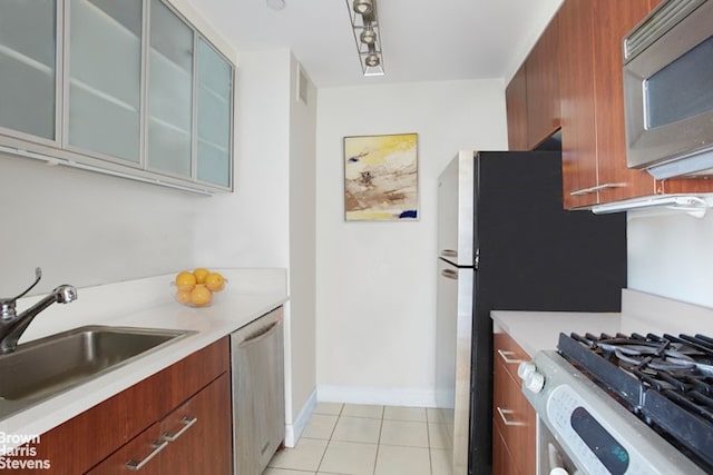 kitchen with light countertops, stainless steel dishwasher, glass insert cabinets, brown cabinetry, and a sink