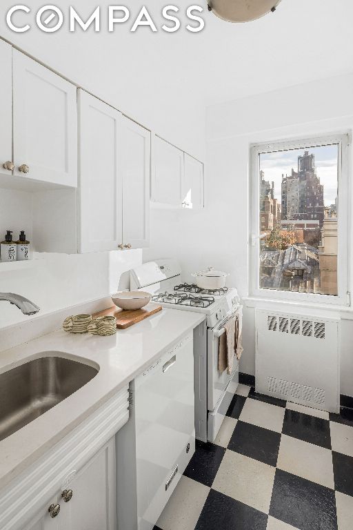 kitchen with white appliances, sink, white cabinets, and radiator heating unit