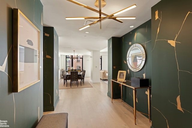 hall featuring light wood-style flooring and an inviting chandelier