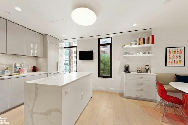 kitchen with light wood finished floors, white cabinets, modern cabinets, a kitchen island, and light stone counters