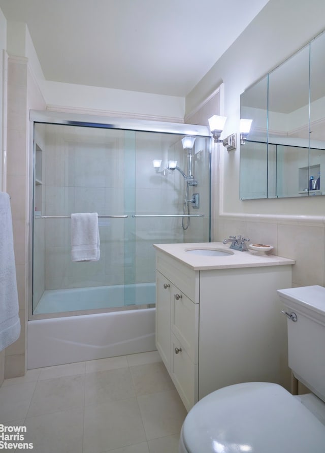 full bath featuring toilet, tile walls, vanity, combined bath / shower with glass door, and tile patterned floors