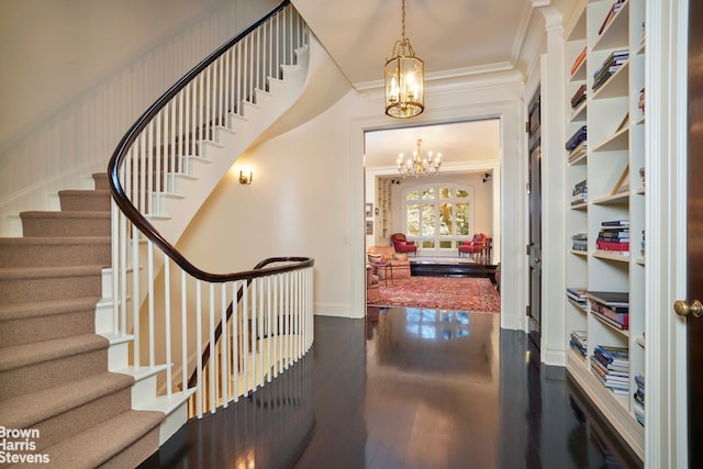 foyer featuring a chandelier, wood finished floors, baseboards, stairs, and ornamental molding