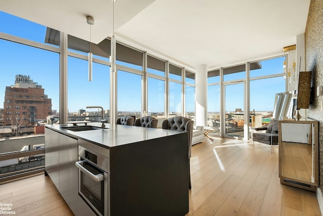 kitchen featuring light wood-style flooring, a city view, oven, expansive windows, and pendant lighting