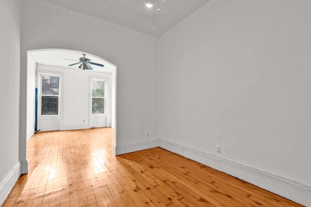 empty room featuring light wood-style floors, baseboards, arched walkways, and a ceiling fan