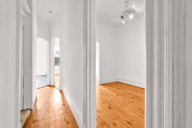 hall featuring arched walkways, wood-type flooring, and baseboards