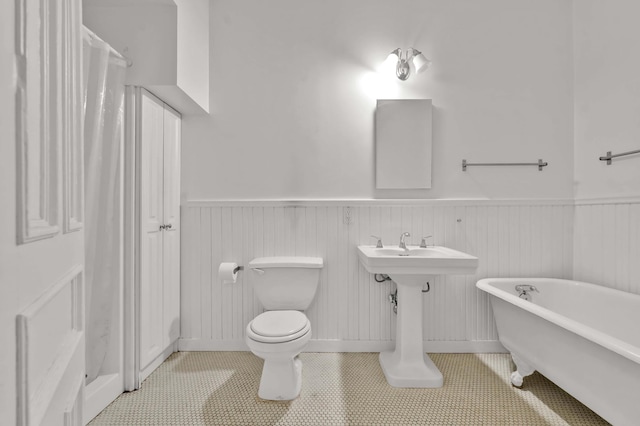 bathroom with toilet, a freestanding tub, tile patterned flooring, and wainscoting