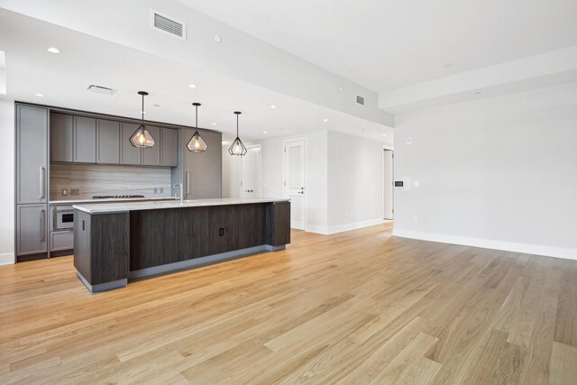 kitchen featuring a large island with sink, pendant lighting, oven, light hardwood / wood-style floors, and backsplash