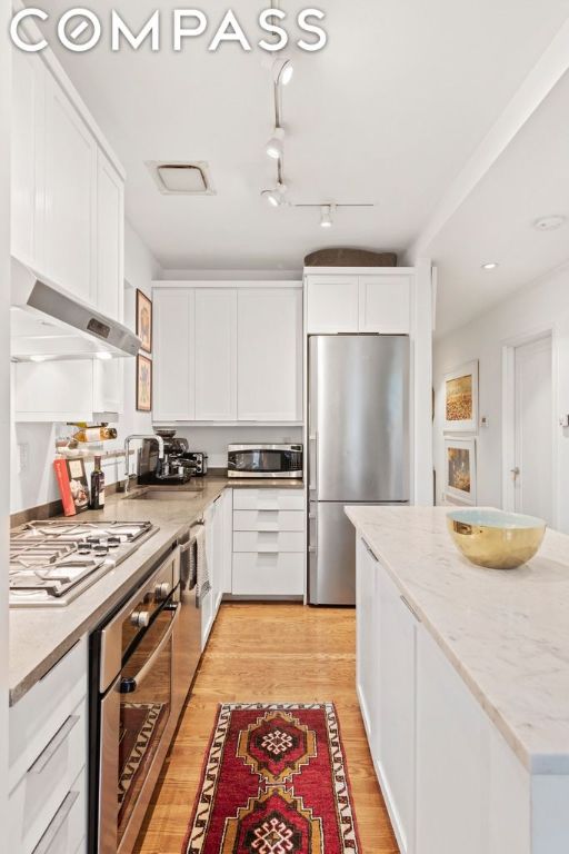 kitchen featuring ventilation hood, stainless steel appliances, white cabinets, light hardwood / wood-style flooring, and sink