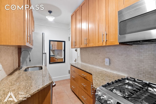 kitchen featuring light tile patterned floors, a sink, light stone countertops, stainless steel appliances, and backsplash