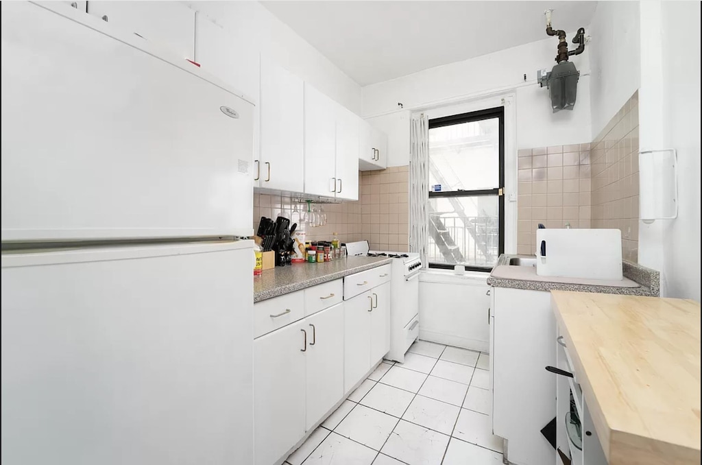 kitchen with white appliances, tasteful backsplash, light tile patterned floors, white cabinets, and butcher block countertops