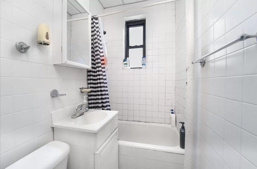 bathroom featuring tiled shower / bath, toilet, vanity, and tile walls