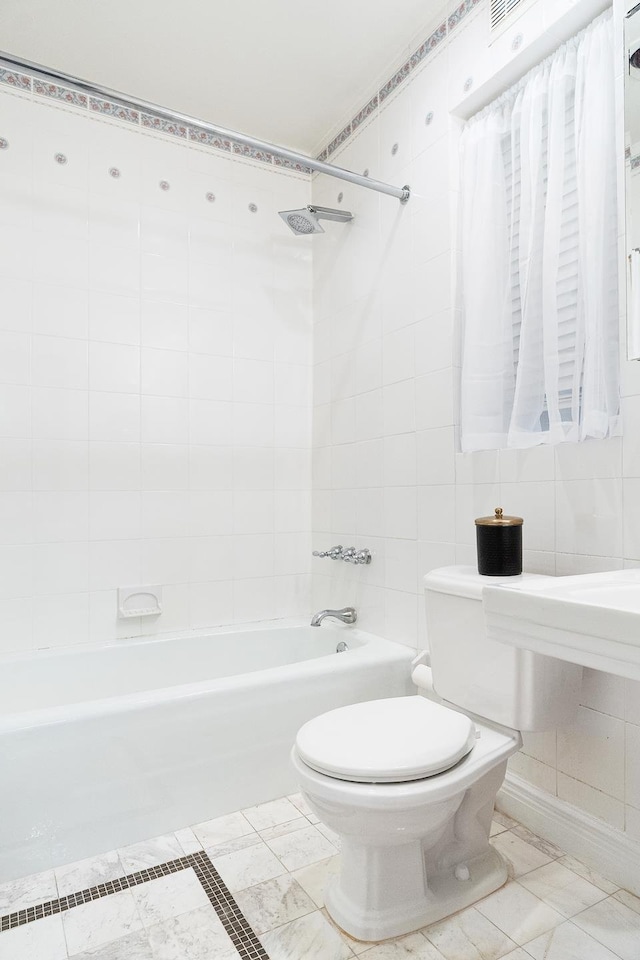 bathroom featuring toilet, marble finish floor, tile walls, and bathing tub / shower combination