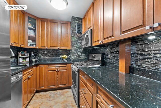 kitchen with brown cabinets, tasteful backsplash, appliances with stainless steel finishes, glass insert cabinets, and dark stone countertops