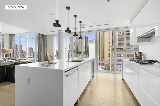 kitchen featuring a wall of windows, an island with sink, hanging light fixtures, and white cabinets