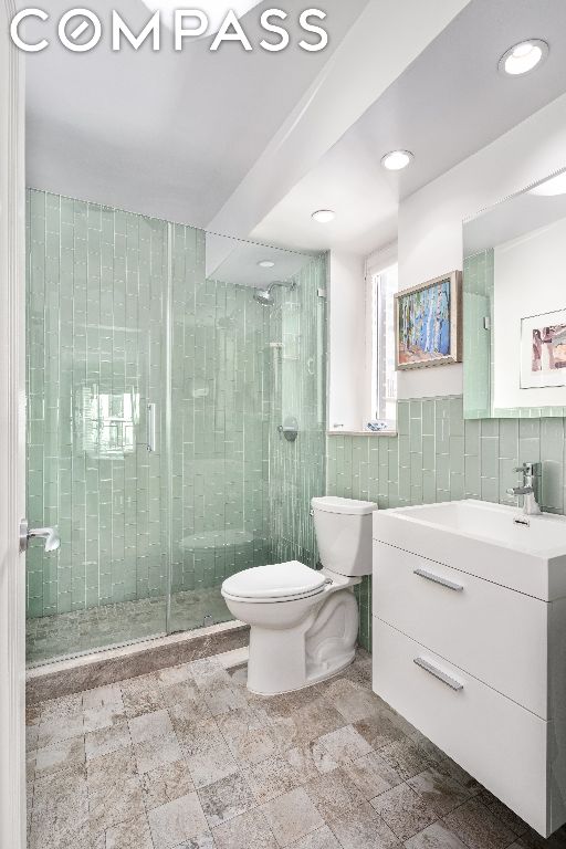 bathroom with toilet, vanity, tasteful backsplash, and a shower with shower door