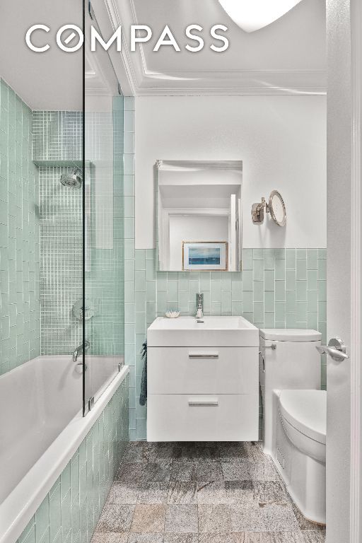 full bathroom featuring toilet, crown molding, tile walls, and tiled shower / bath