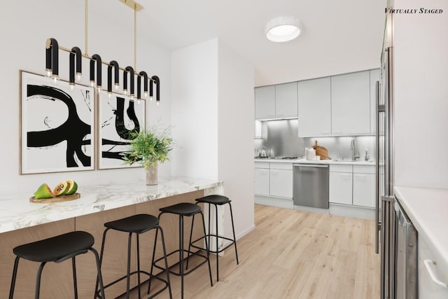 kitchen featuring dishwasher, a breakfast bar, sink, light hardwood / wood-style flooring, and white cabinets