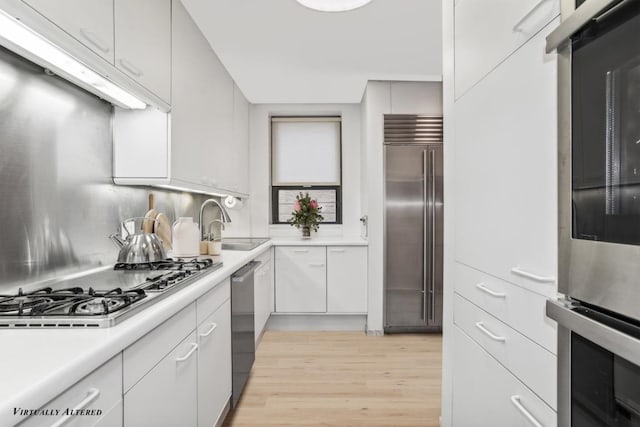 kitchen with white cabinetry, stainless steel appliances, tasteful backsplash, light hardwood / wood-style floors, and sink