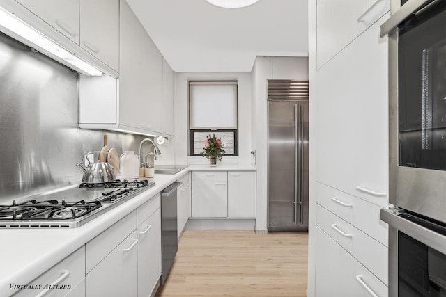 kitchen featuring light wood finished floors, light countertops, appliances with stainless steel finishes, white cabinets, and a sink