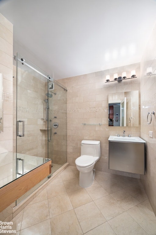 bathroom with toilet, a shower with shower door, tile walls, vanity, and tile patterned flooring