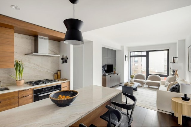 kitchen featuring black oven, tasteful backsplash, stainless steel gas stovetop, light stone counters, and wall chimney range hood