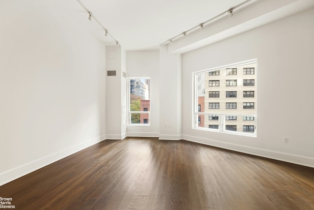 empty room with visible vents, dark wood finished floors, and track lighting