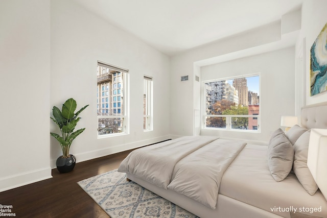 bedroom featuring a view of city, baseboards, and dark wood finished floors