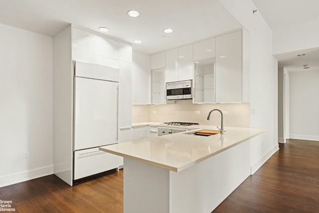 kitchen with paneled built in refrigerator, a peninsula, white cabinetry, light countertops, and stainless steel microwave