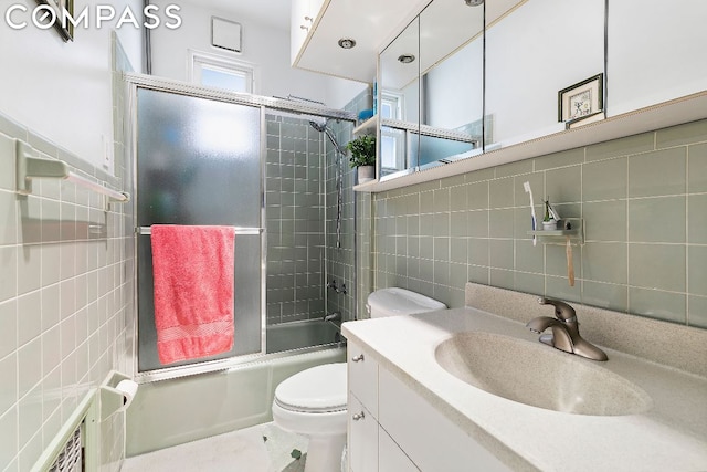 full bathroom featuring shower / bath combination with glass door, vanity, tasteful backsplash, tile walls, and toilet