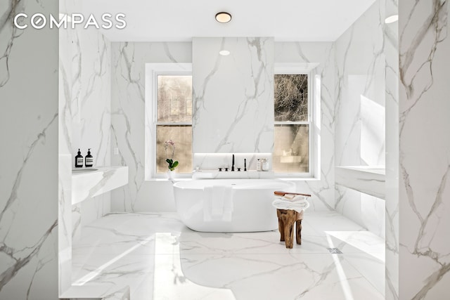 bathroom featuring marble finish floor, a freestanding bath, and stone wall