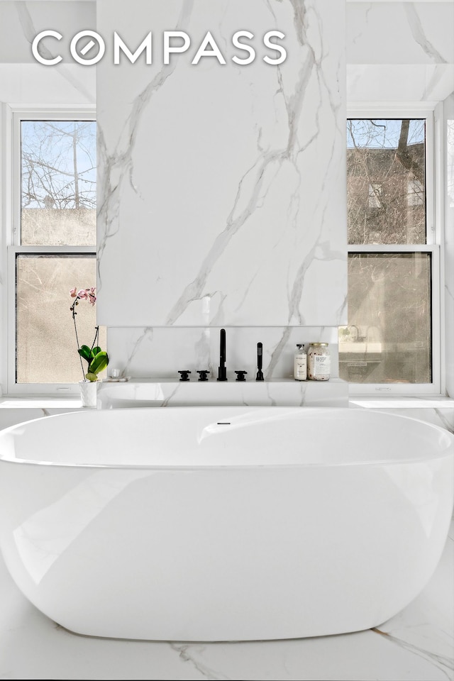 bathroom featuring stone wall, a freestanding bath, and marble finish floor