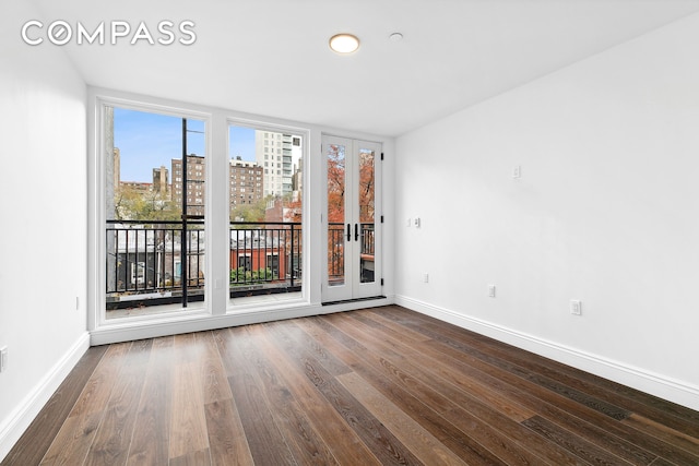 unfurnished room featuring baseboards, a city view, and dark wood-style floors