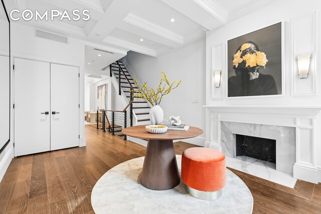 dining space with coffered ceiling, beamed ceiling, ornamental molding, hardwood / wood-style flooring, and a premium fireplace