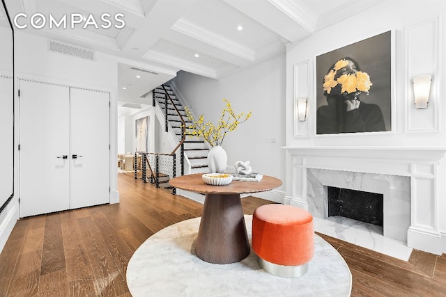 interior space with a premium fireplace, hardwood / wood-style floors, beam ceiling, coffered ceiling, and ornamental molding