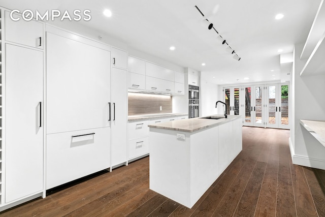 kitchen with an island with sink, a sink, dark wood finished floors, white cabinetry, and decorative backsplash