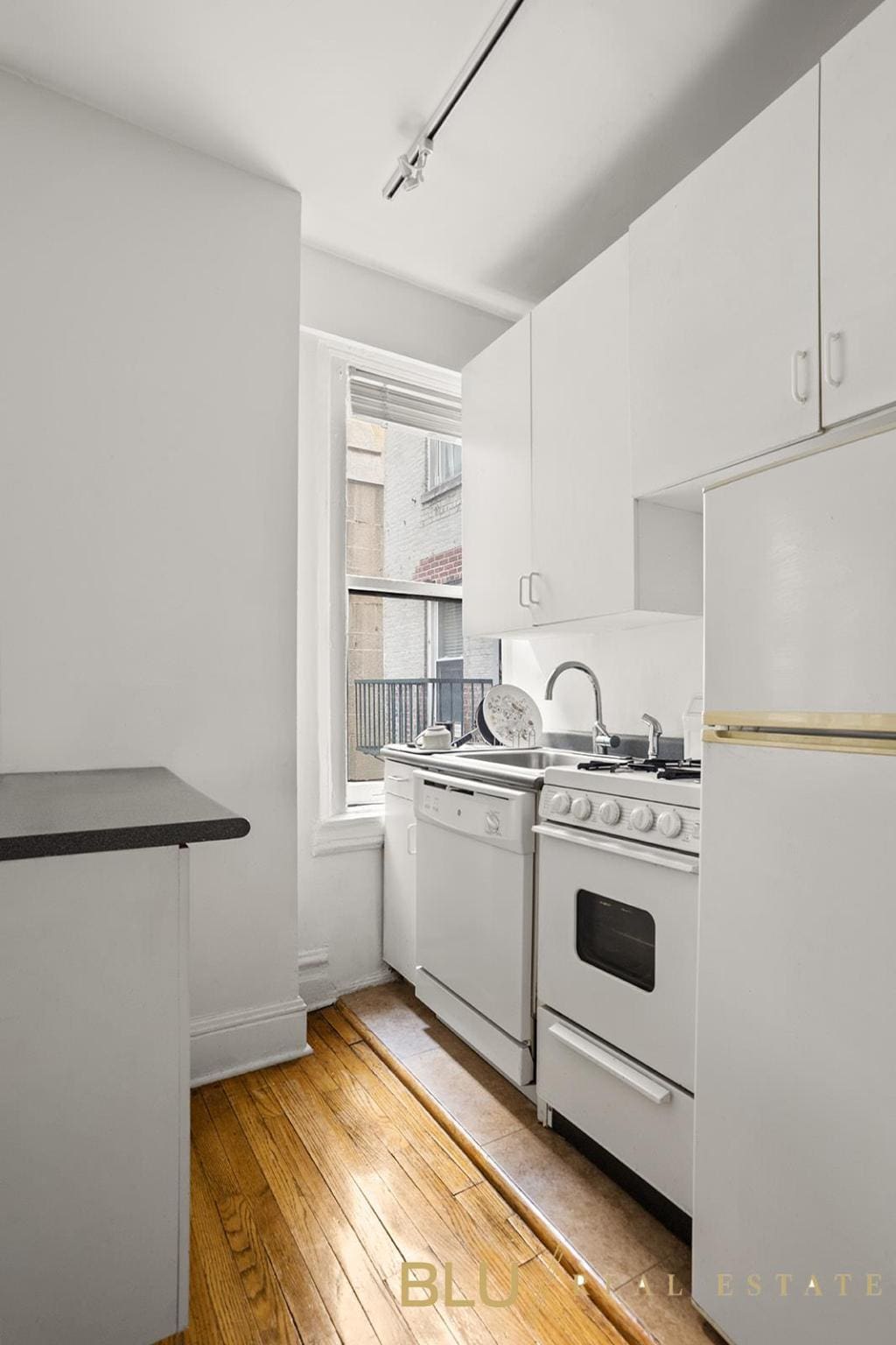 kitchen with dark countertops, white appliances, white cabinets, and hardwood / wood-style flooring