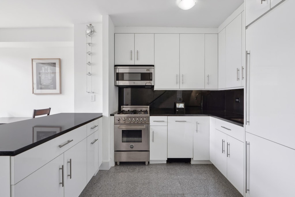 22 W 15th St Unit 7I, New York City, NY 10011 - kitchen featuring a peninsula, dark countertops, white cabinets, decorative backsplash, and stainless steel appliances