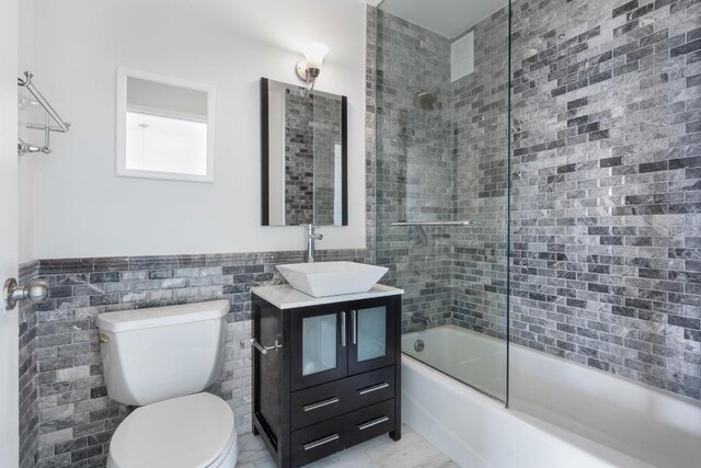 full bathroom with bath / shower combo with glass door, tile walls, vanity, and toilet