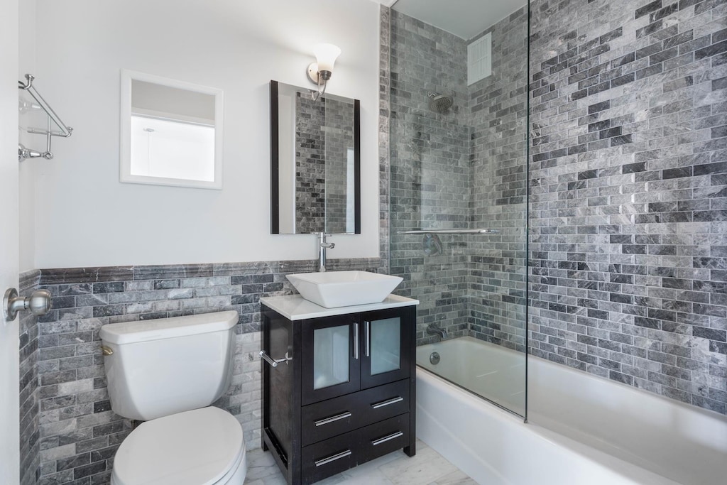 22 W 15th St Unit 7I, New York City, NY 10011 - bathroom with bath / shower combo with glass door, toilet, tile walls, vanity, and a wainscoted wall