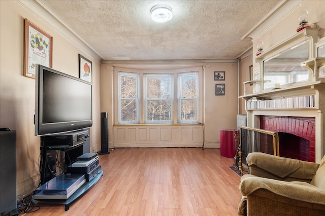 sitting room with a brick fireplace, crown molding, a textured ceiling, and wood finished floors